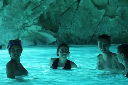 Turistas nadando dentro de la Cueva Azul en Vlora, rodeados de agua turquesa brillante y paredes de piedra caliza iluminadas en la península de Karaburun, Albania.