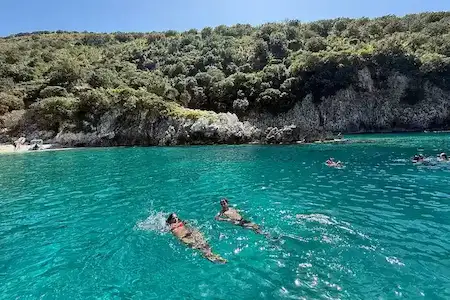 Turistas nadando en las aguas turquesas y transparentes de la bahía de Bristan (Bahía del Oso), en la salvaje península de Karaburun, cerca de la Bahía de Grama, Vlora, Albania.
